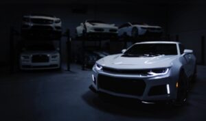 手前に停車された白いスポーツカーと奥のリフトに他の車が見える暗いガレージ